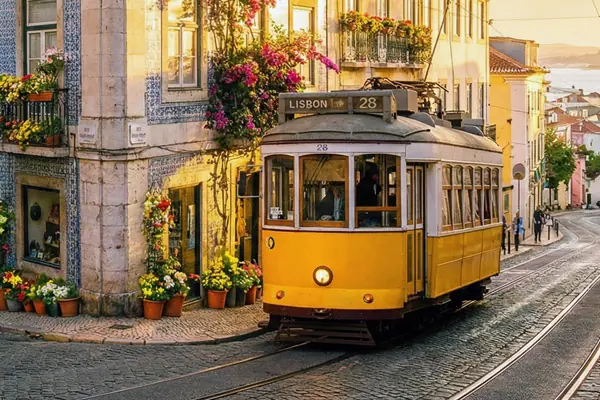 Słynny żółty tramwaj 28 na uliczce w Lizbonie – tło oferty kursów języka portugalskiego (Online i w Katowicach) w Alma Española.