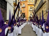 Procesja Semana Santa w Hiszpanii: nazarenos w fioletowych kapturach i białych szatach na wąskiej uliczce.