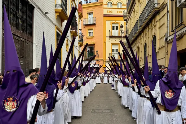 Procesja Semana Santa w Hiszpanii: nazarenos w fioletowych kapturach i białych szatach na wąskiej uliczce.