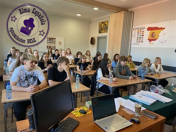 Archiwalne zdjęcie sali szkoleniowej w Katowicach z grupą kursantów podczas pisania egzaminu językowego DELE w ośrodku Alma Española. W lewym górnym rogu cyfrowy stempel oficjalnego egzaminatora.